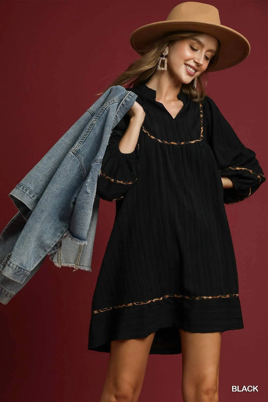Plus-size black textured babydoll dress with leopard trim, modeled with denim jacket and hat.