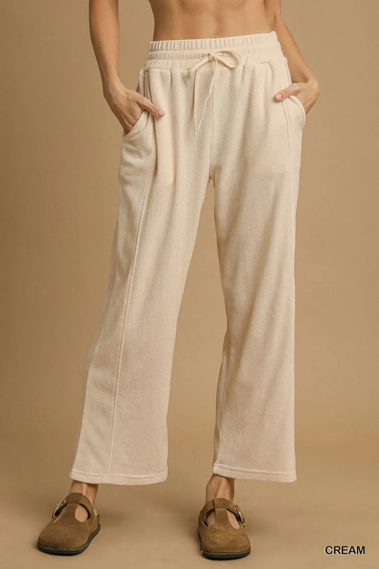 Cream drawstring wide-leg pants with flowy fit, side pockets, and adjustable waistband.