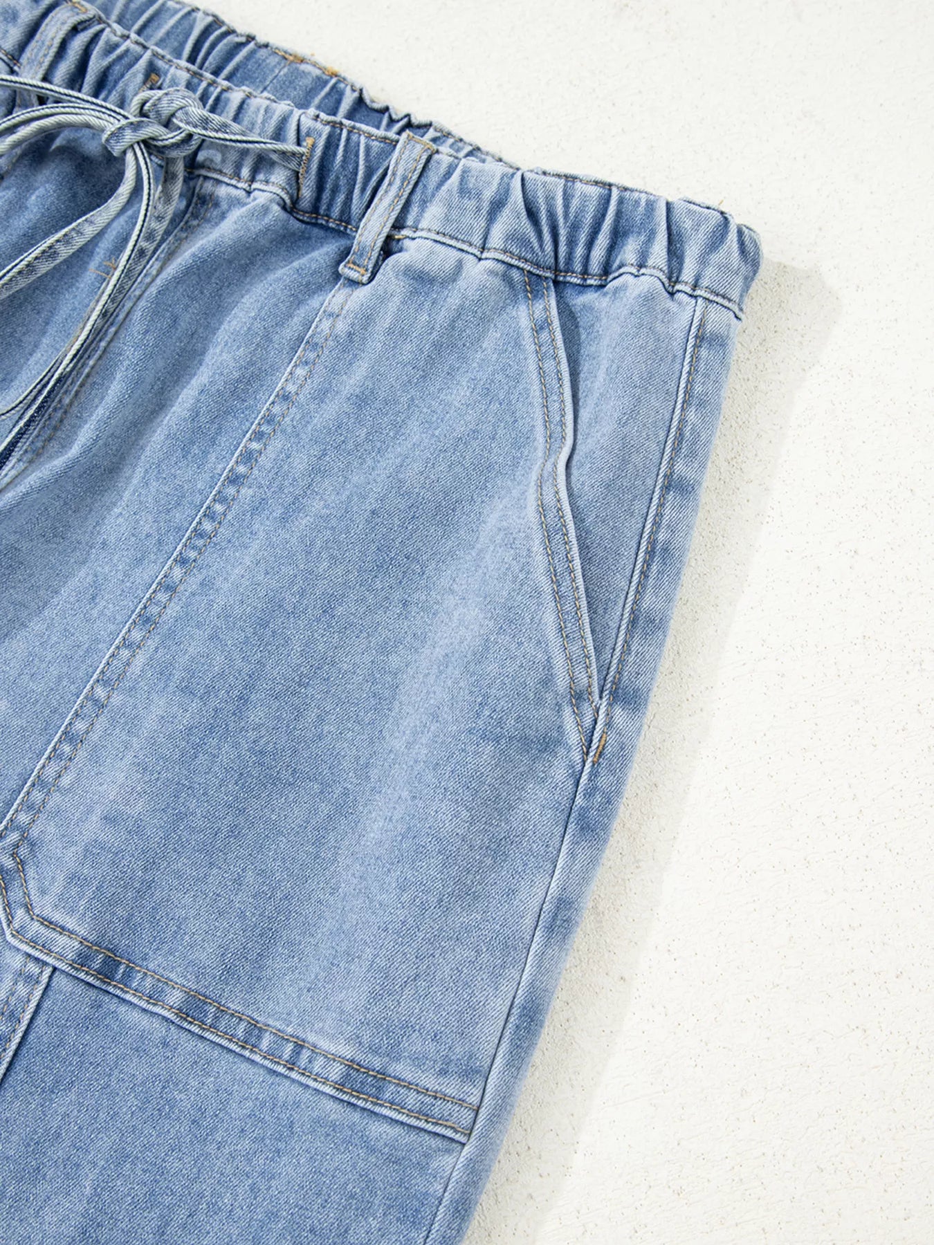Close-up of light wash wide-leg jeans with drawstring waist and raw hem.