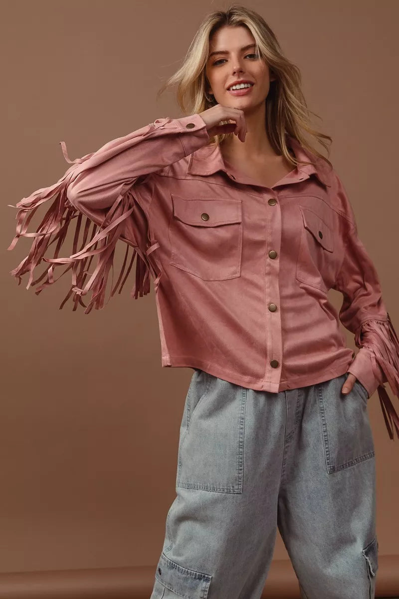Blonde model wearing pink suede fringe long sleeve jacket with collar and buttons, paired with gray cargo pants.