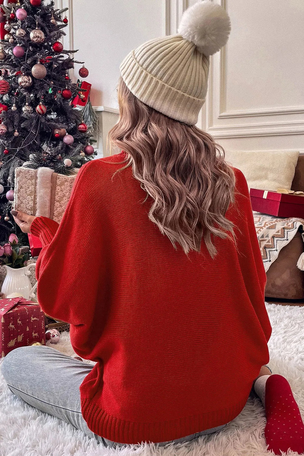 Woman in emerald green turtleneck sweater with ribbed texture, sitting by Christmas tree.