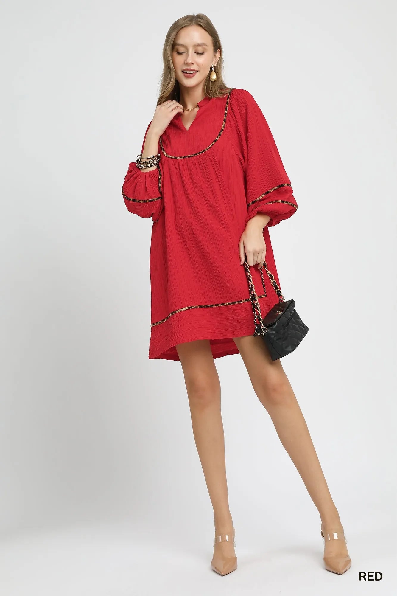 Woman in red textured babydoll dress with leopard trim, holding black bag.