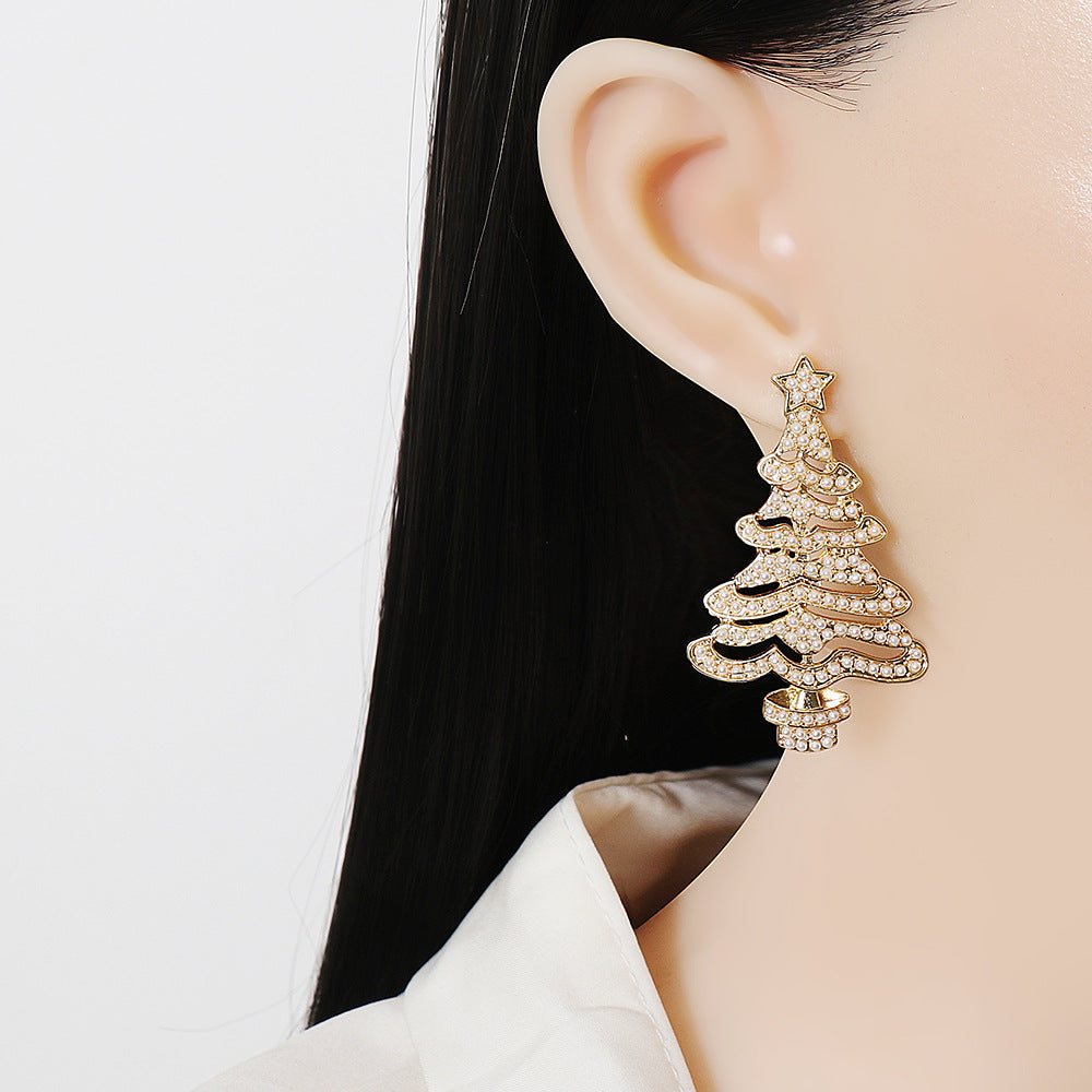 Gold alloy Christmas tree earrings with rhinestones, worn as studs on a model.