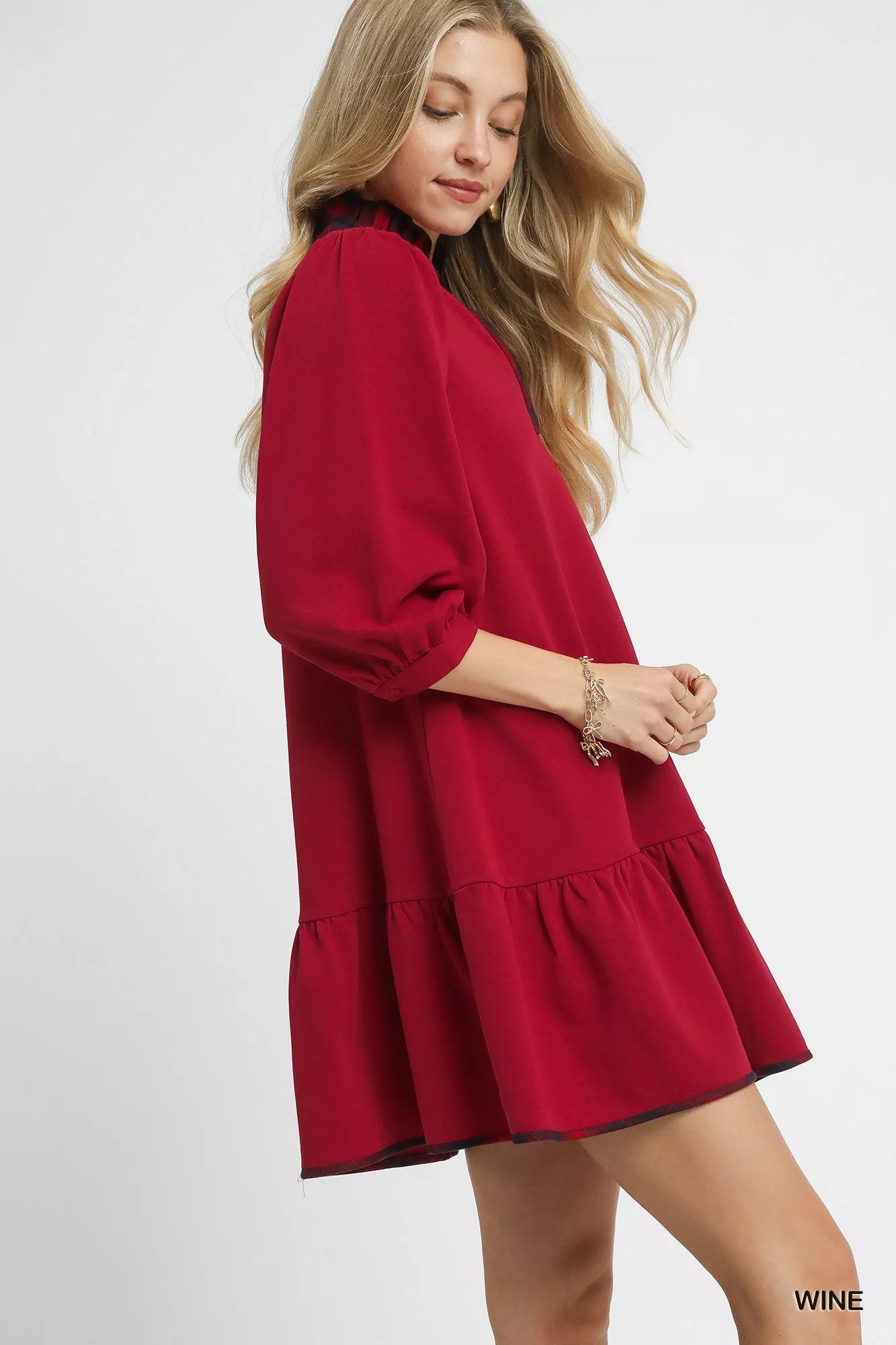 Woman modeling a red French terry ruffle hem dress with black plaid trim.