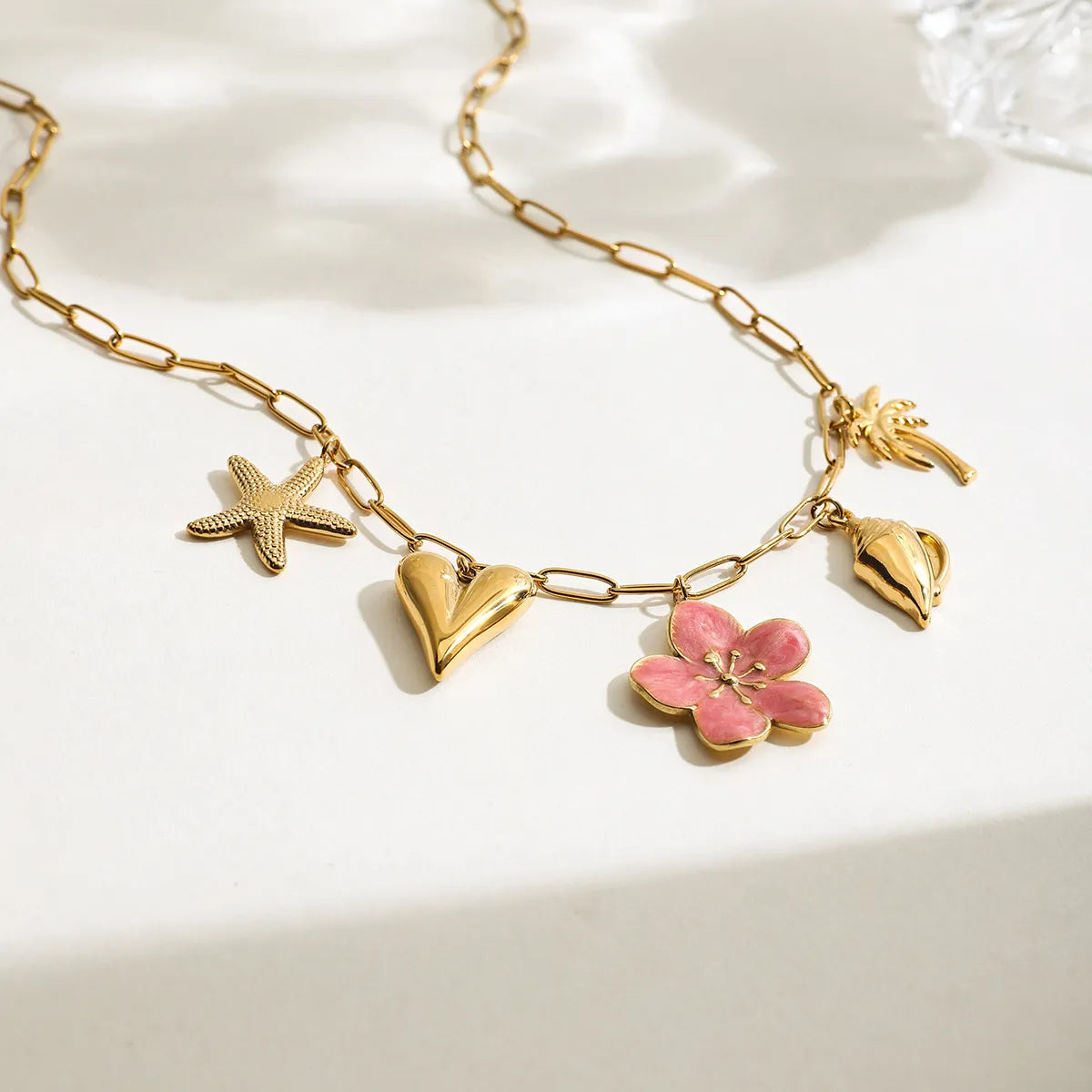Gold-toned chain necklace with pink resin flower, starfish, heart, seashell, and palm charms.