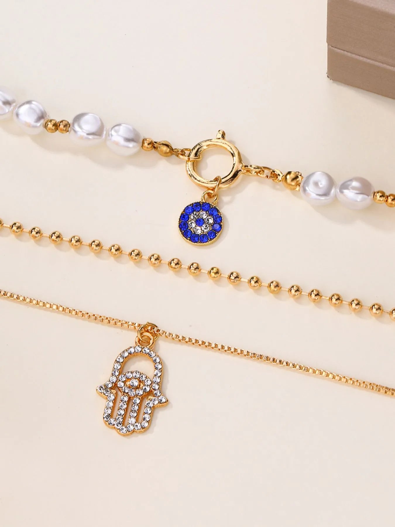Layered 18K gold-plated necklace with pearl strands, evil eye, and hamsa charms.