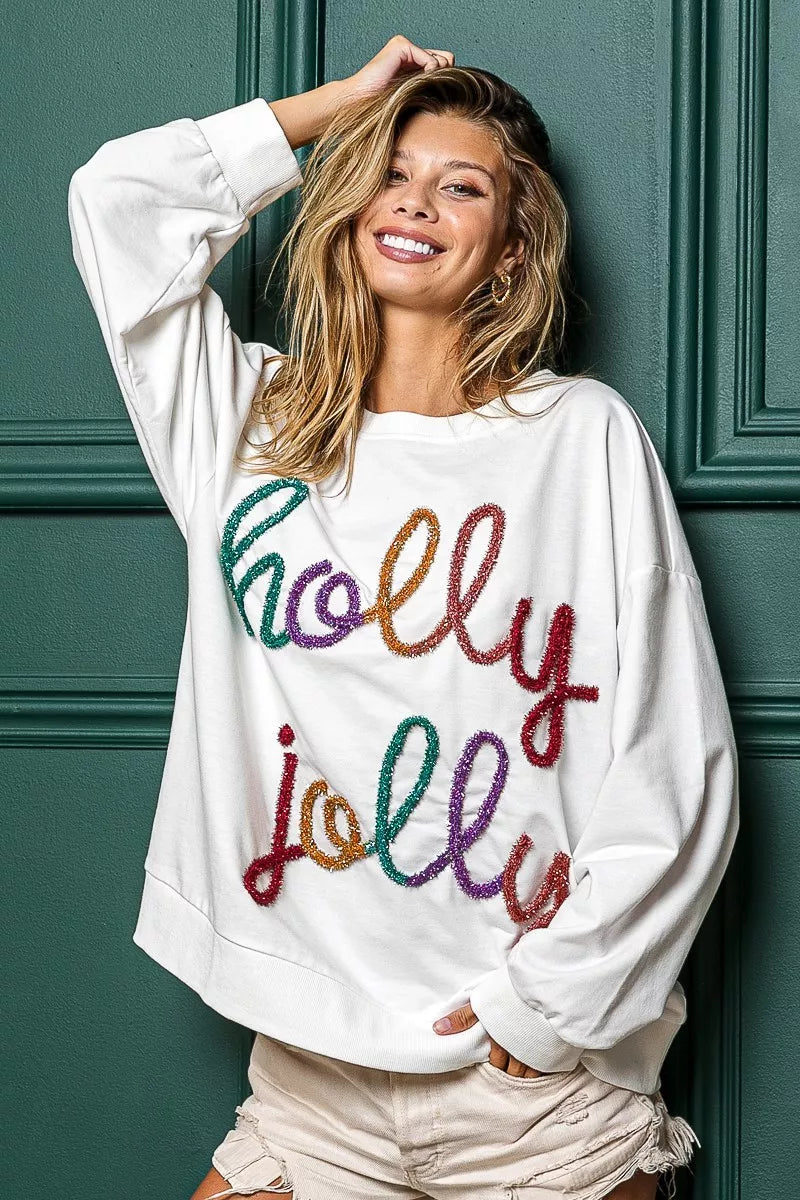 White oversized French terry sweatshirt with colorful "Holly Jolly" graphic.