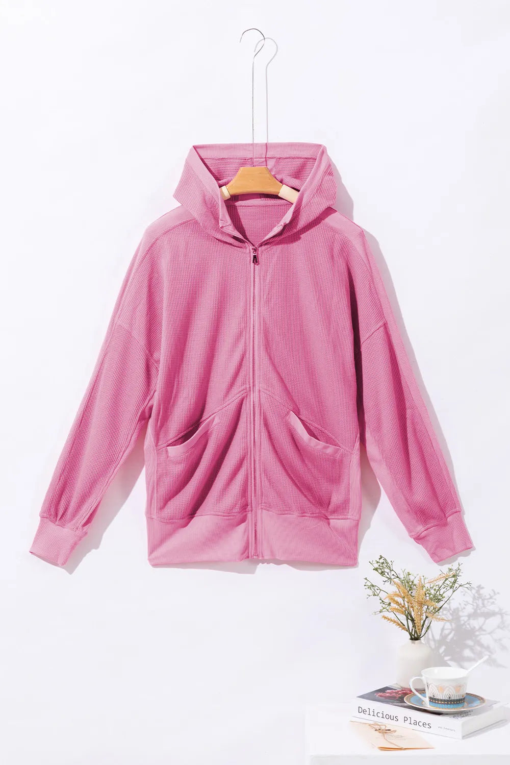 Soft pink waffle-knit zip-up hooded jacket with pockets, hanging on a hook.