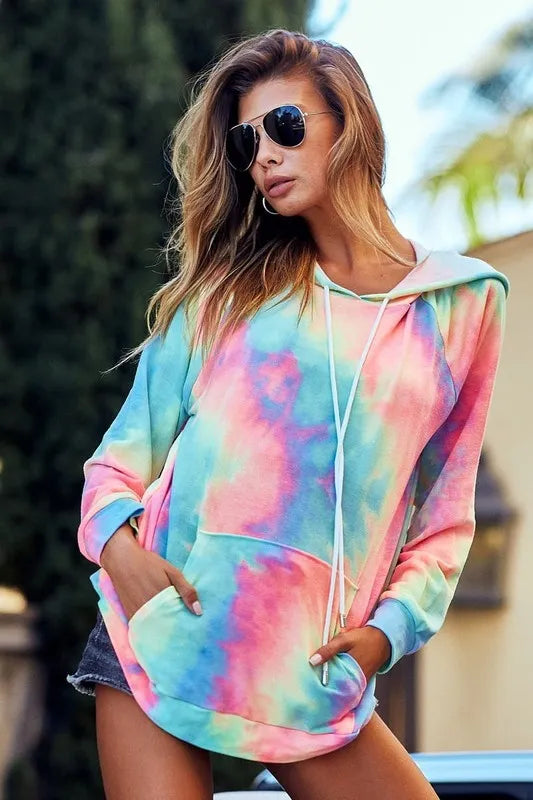 Woman modeling a vibrant tie-dye French terry hoodie with kangaroo pocket and drawstring hood.
