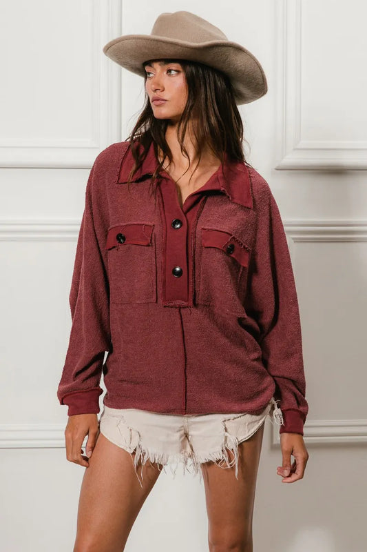 Oversized maroon French terry collared top with buttons and pockets, modeled with a beige cowboy hat and frayed shorts.