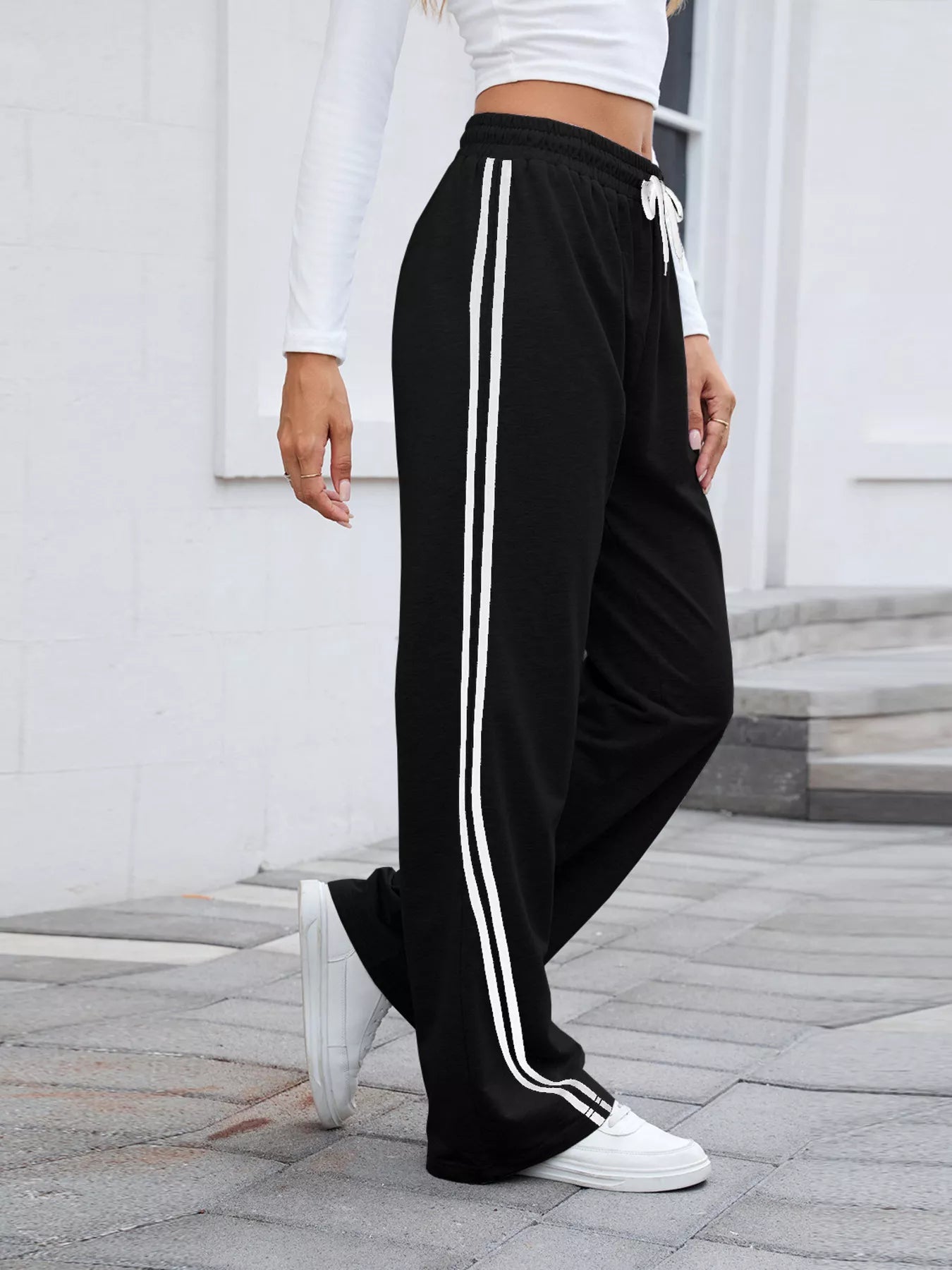 Woman modeling black wide-leg pants with white side stripes and drawstring waist.