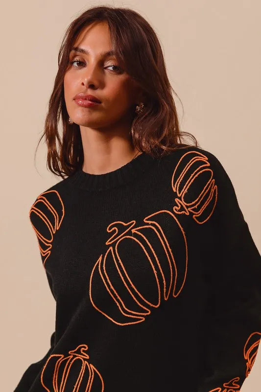 Black knit sweater with orange embroidered pumpkin motifs on a model.