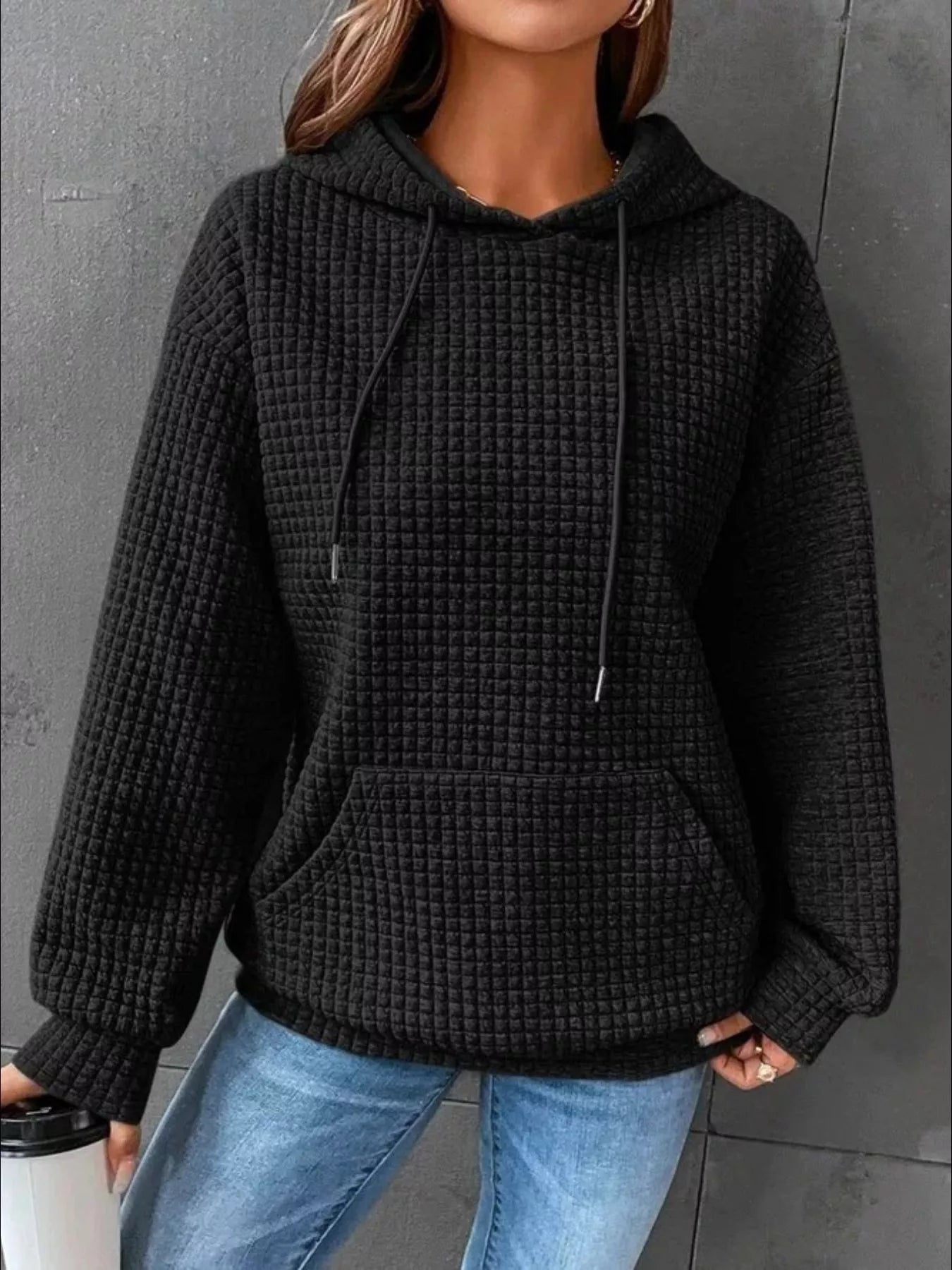Black waffle knit hoodie with drawstring hood and front pocket, modeled on a woman.
