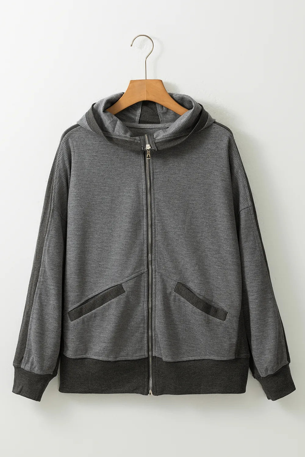 Soft pink waffle-knit zip-up hooded jacket with pockets, hanging on a wooden hanger.