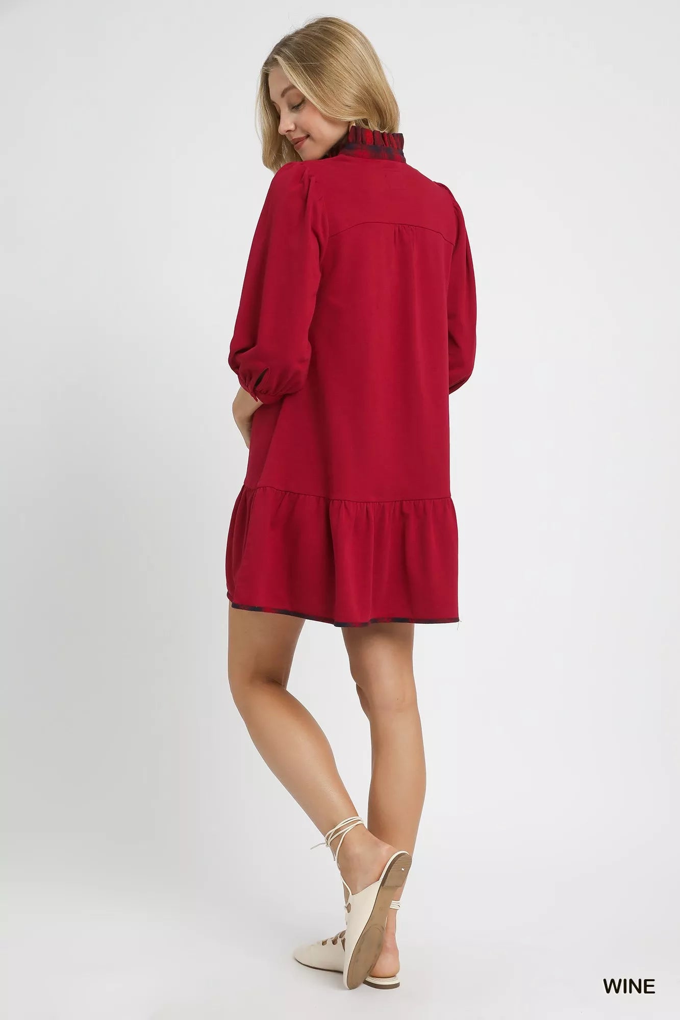 Rear view of red French terry ruffle hem dress with plaid trim on model.