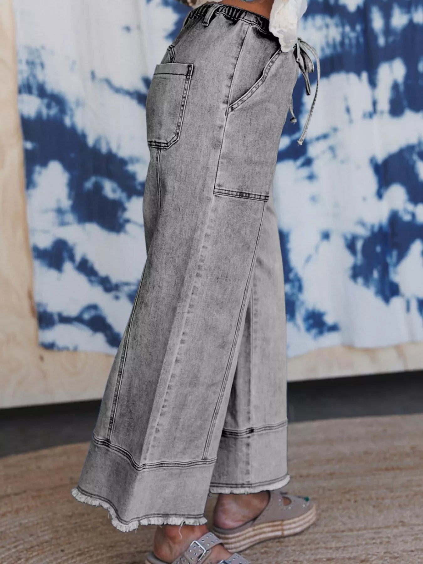 Light wash wide-leg jeans with drawstring waist and raw hem on model.