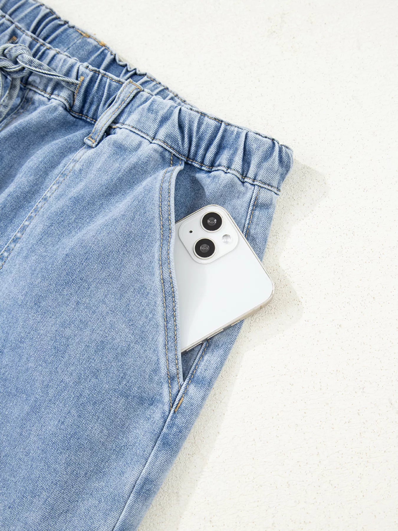 Light wash wide-leg drawstring jeans with raw hem and a phone in the pocket.