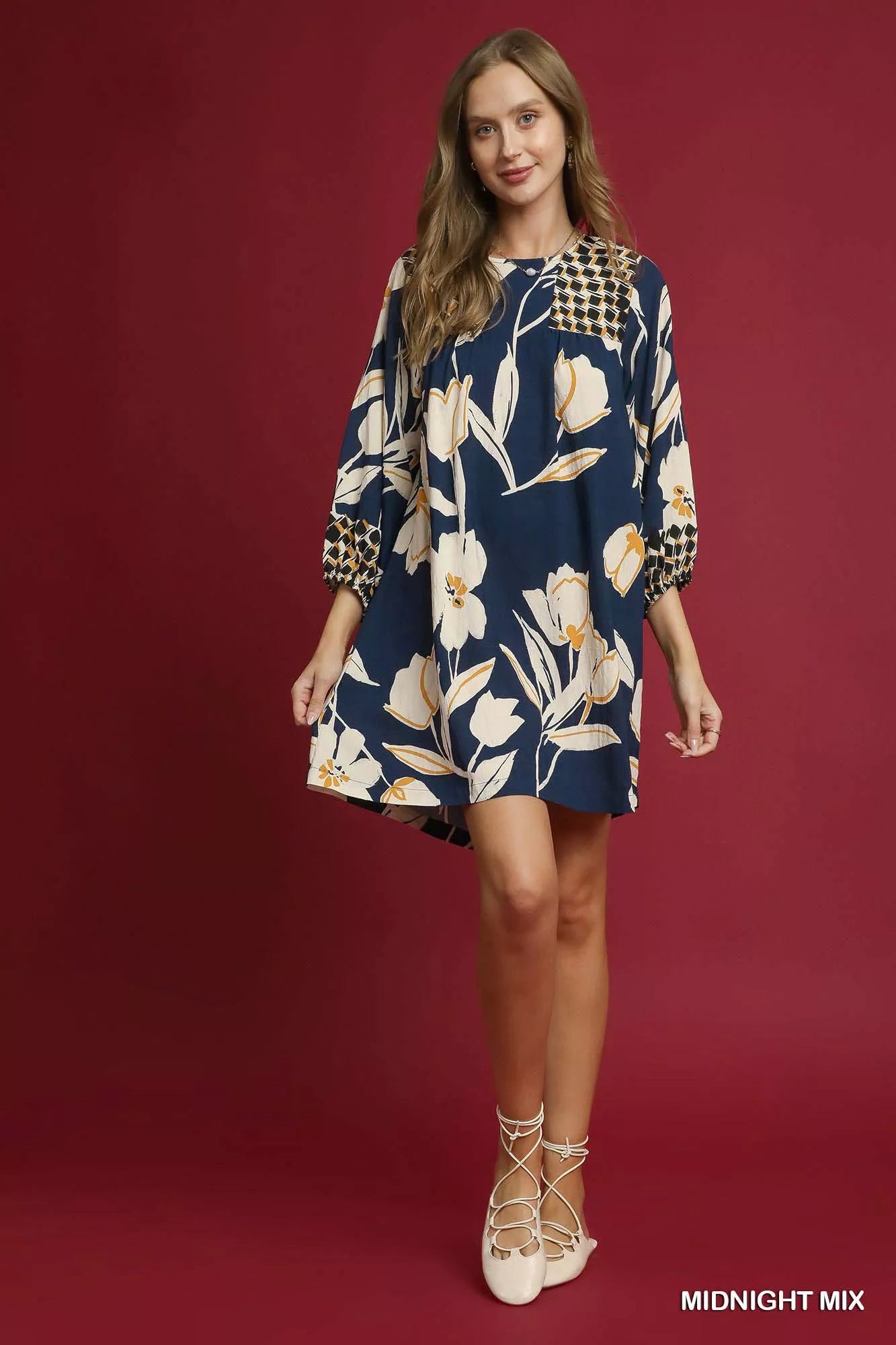 Woman modeling a navy floral high-low babydoll dress with puffed sleeves on red background.