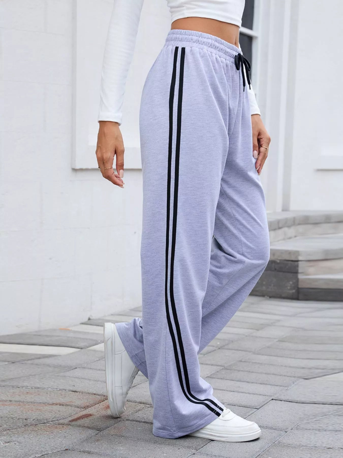 Gray wide-leg pants with black side stripes and drawstring waist, modeled on a person.