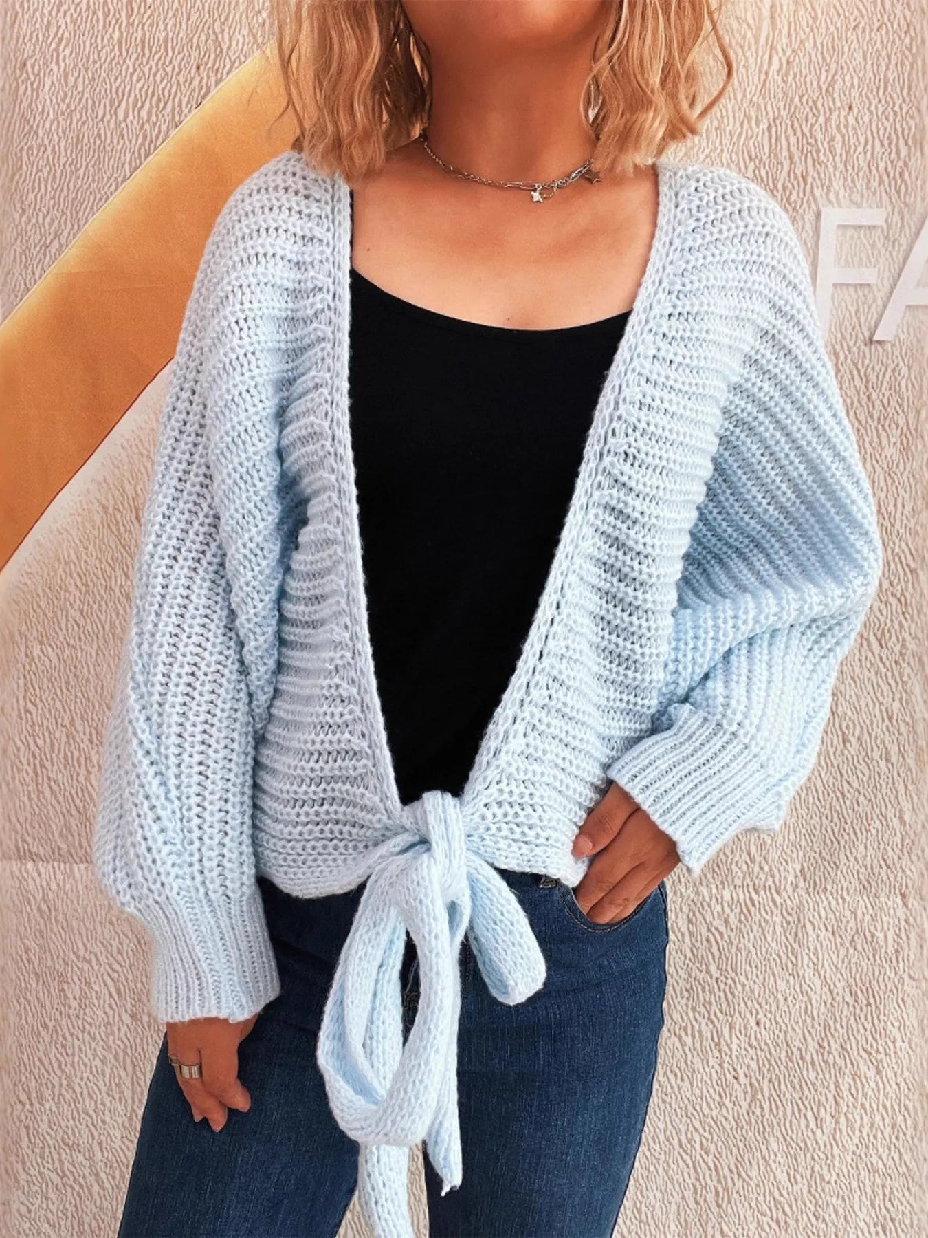Light blue long-sleeve cardigan with tie front, worn open over a black top and jeans.
