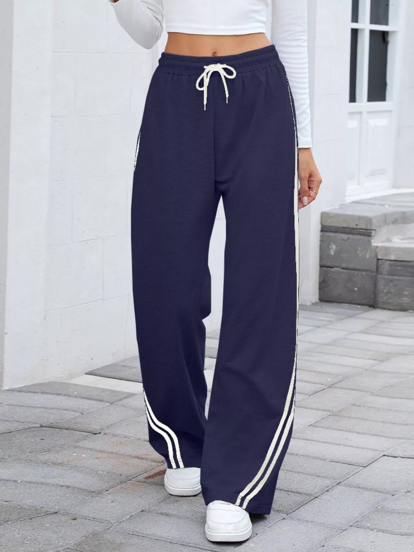 Navy wide-leg pants with white side stripes and drawstring waist, modeled on a person.