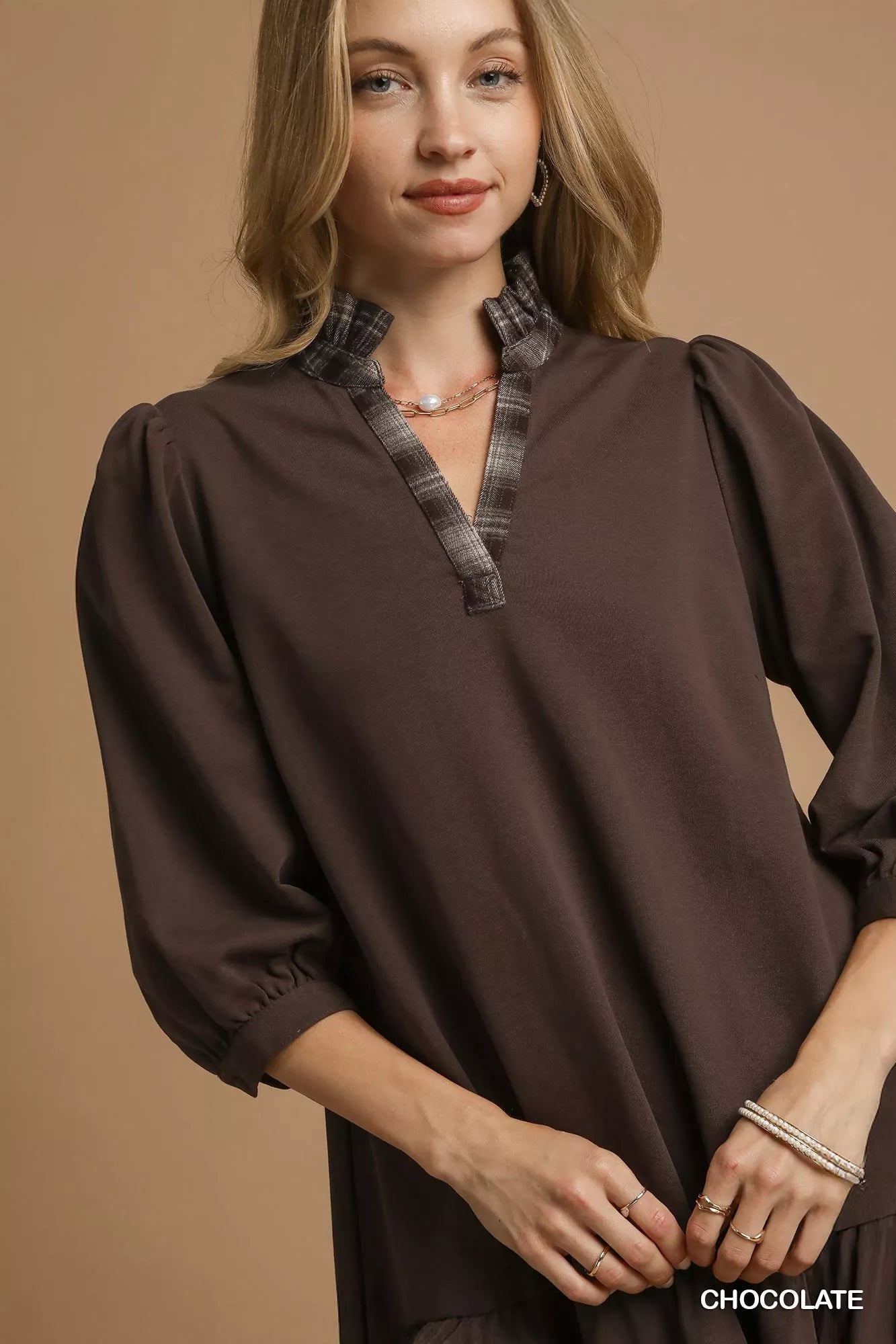 Woman modeling a brown French terry dress with ruffle hem and plaid trim.