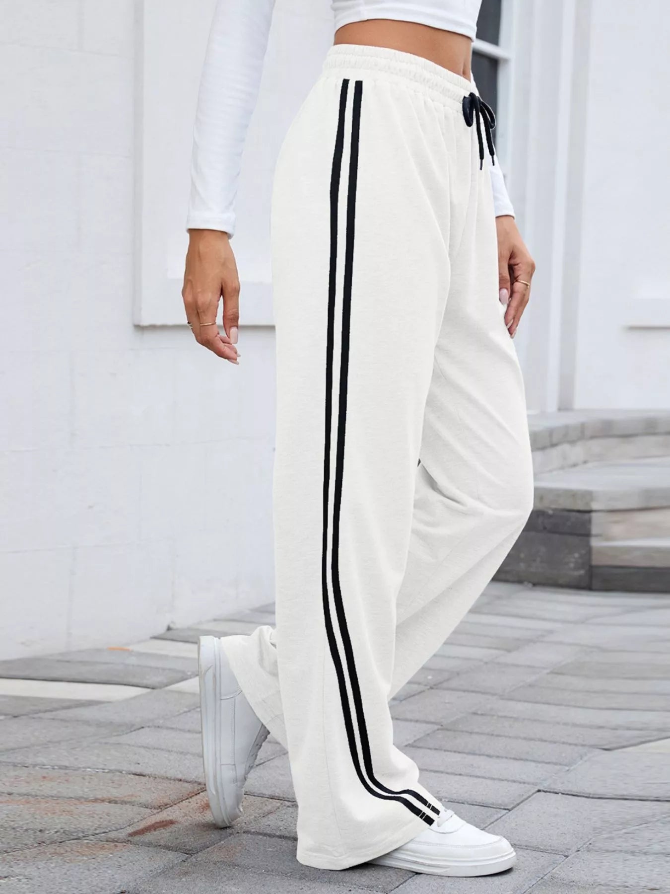White wide-leg pants with black side stripes and drawstring waist, modeled by a woman.