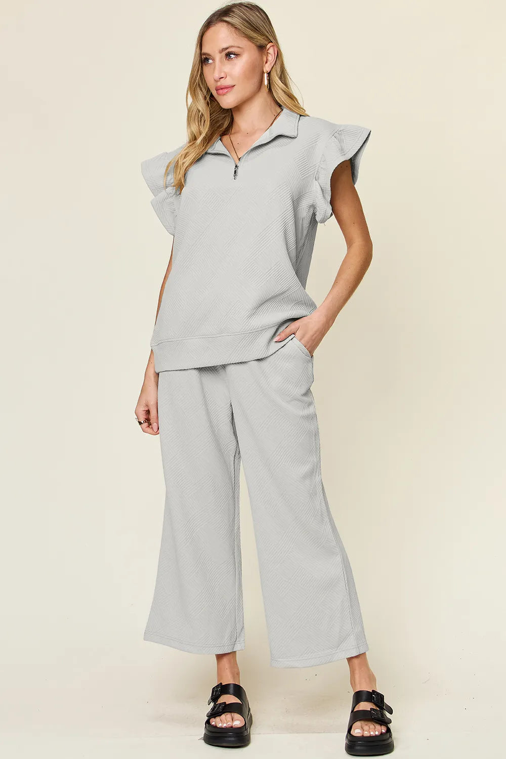 Gray textured ruffle short sleeve top with zipper and wide leg pants set on model.