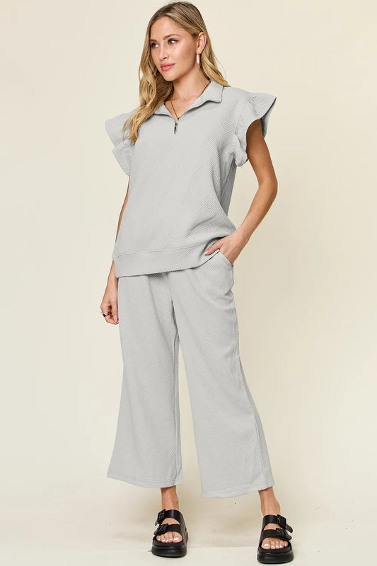 Gray textured ruffle short sleeve top with zipper and wide leg pants set on model.