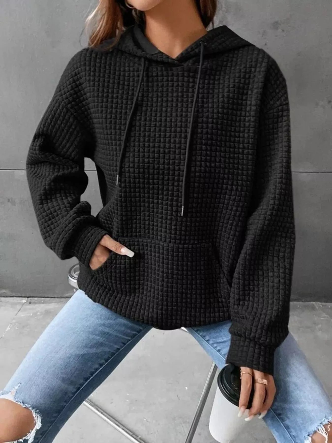 Black waffle knit hoodie with drawstring hood and front pocket, modeled on a woman.