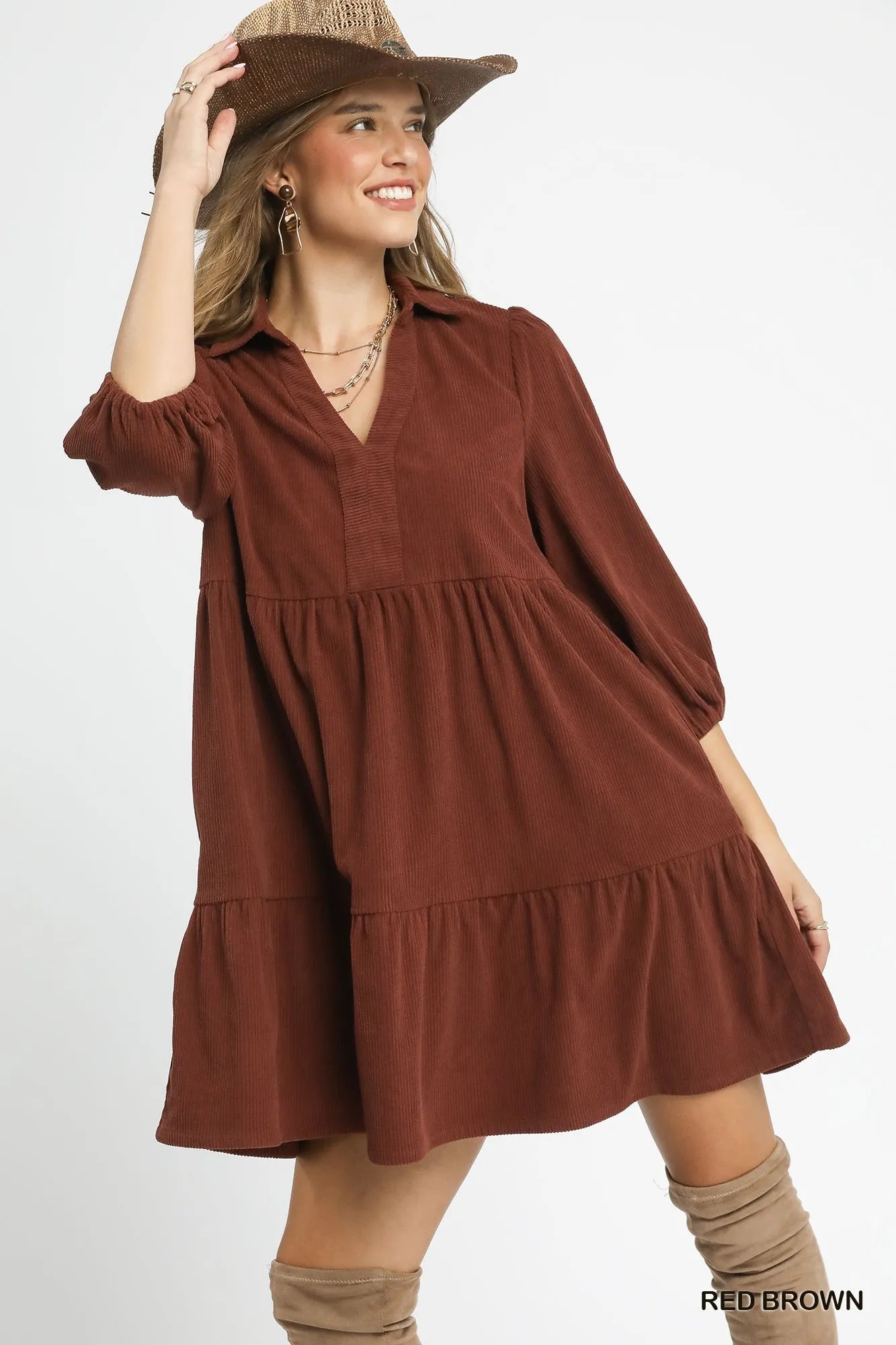 Woman modeling a rust-colored tiered corduroy mini dress with balloon sleeves, V-neck, and wide-brim hat.