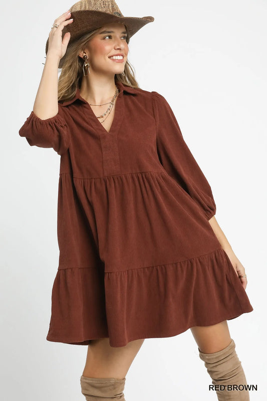 Woman modeling a rust-colored tiered corduroy mini dress with balloon sleeves, V-neck, and wide-brim hat.