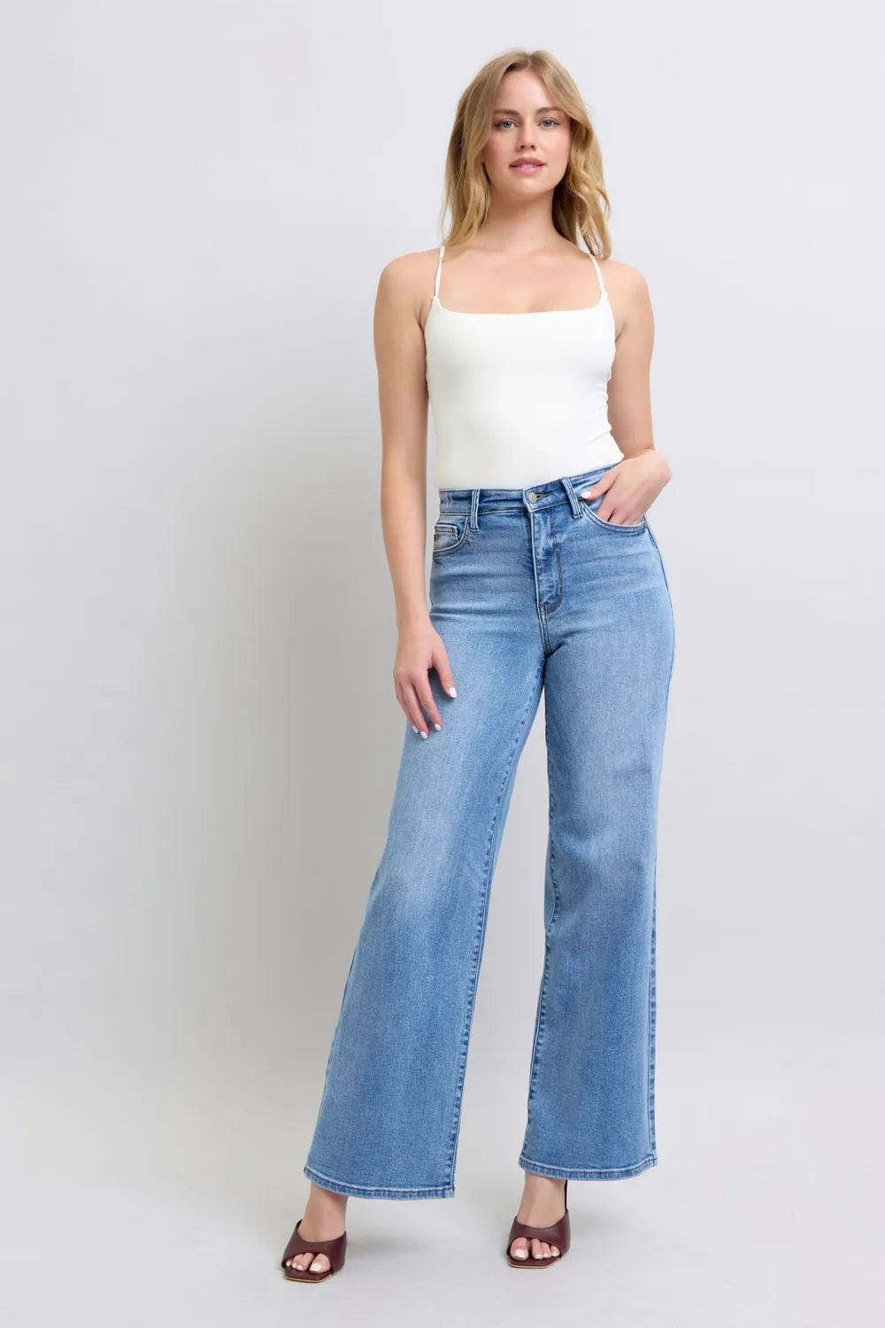 Model poses in Judy Blue high-waist wide-leg jeans with pockets, paired with a white camisole and maroon sandals.