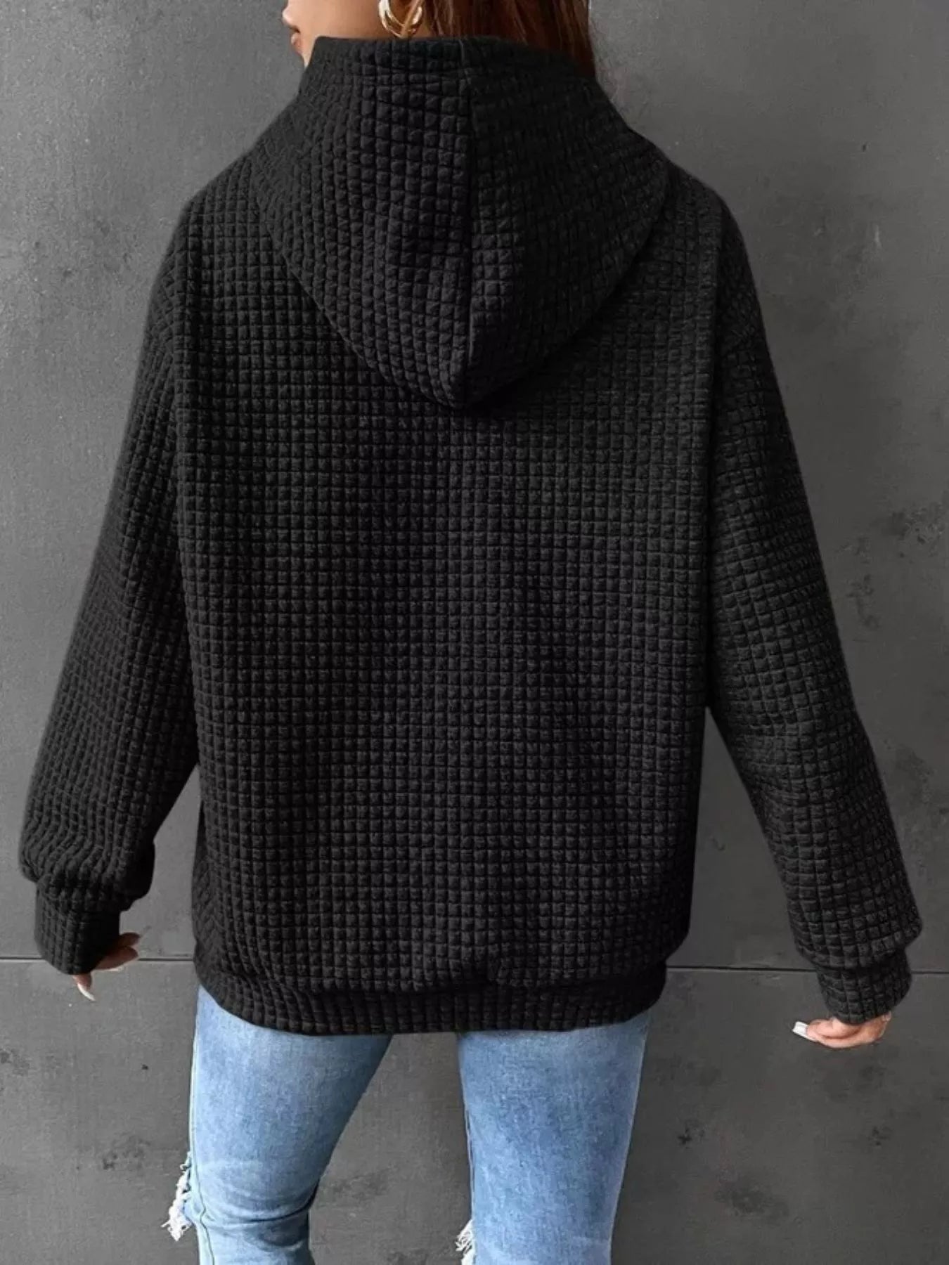 Black waffle knit hoodie with drawstring hood and pockets, worn by model from behind.