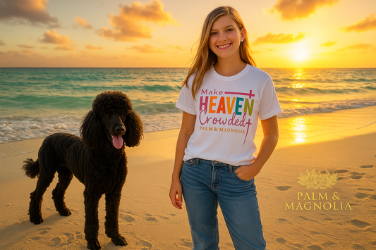 White USA-made cotton T-shirt with rainbow "Make Heaven Crowded" text, modeled by a smiling young woman with a black poodle on a sunny beach.