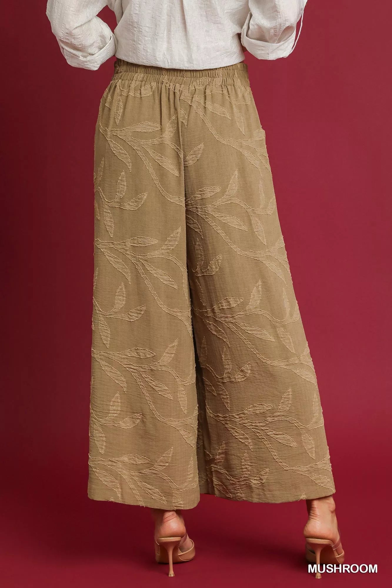 Rear view of beige jacquard wide-leg pants with leaf patterns, paired with a white blouse and heels.