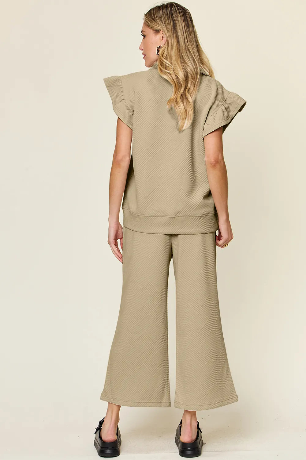Rear view of a woman modeling a textured ruffle short sleeve top and wide leg pants set in beige.