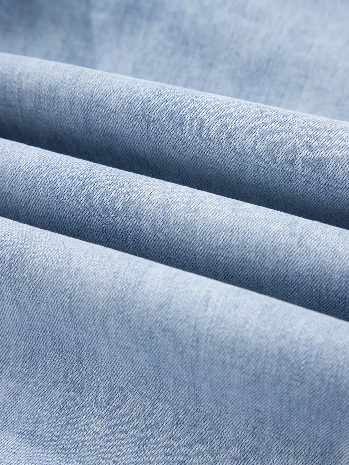 Close-up of light wash denim fabric from wide leg drawstring raw hem jeans.