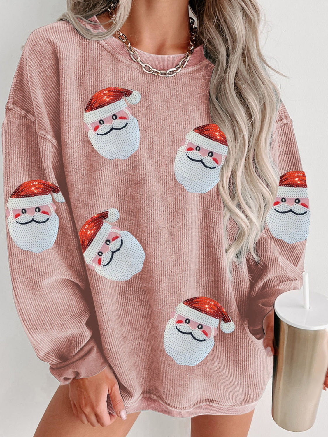 Ribbed sweatshirt in pink with sequin Santa patches and a model holding a tumbler.