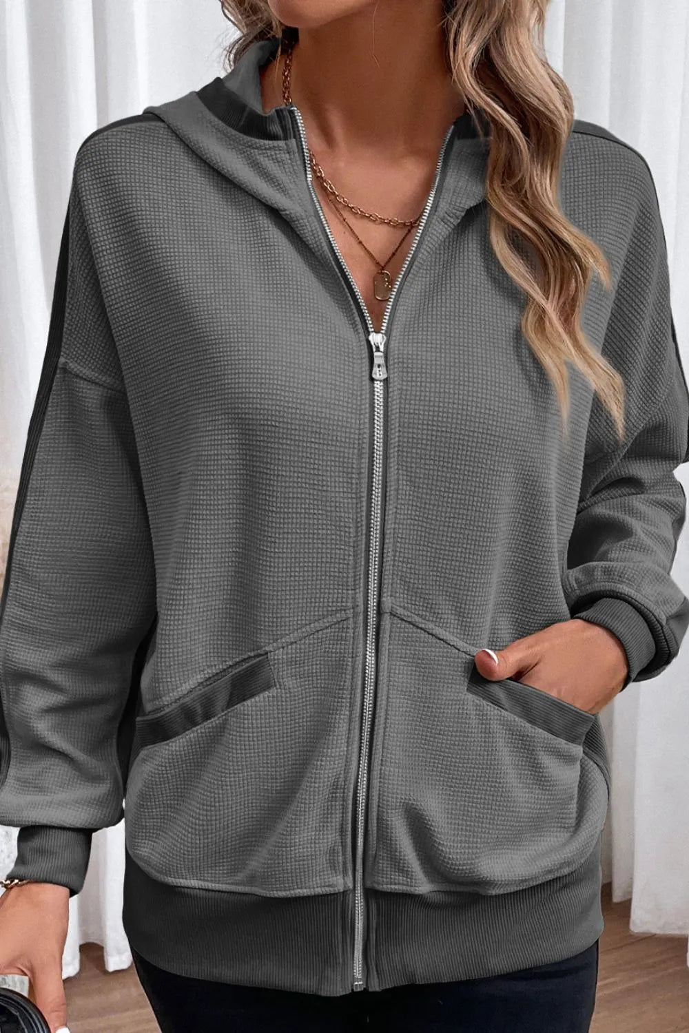 Woman wearing a soft pink waffle-knit zip-up hooded jacket with pockets.