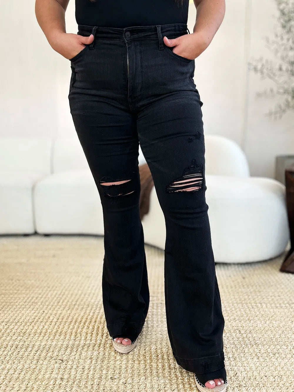 Black high-waist distressed flare jeans on a model, with rips on thighs and flared legs.