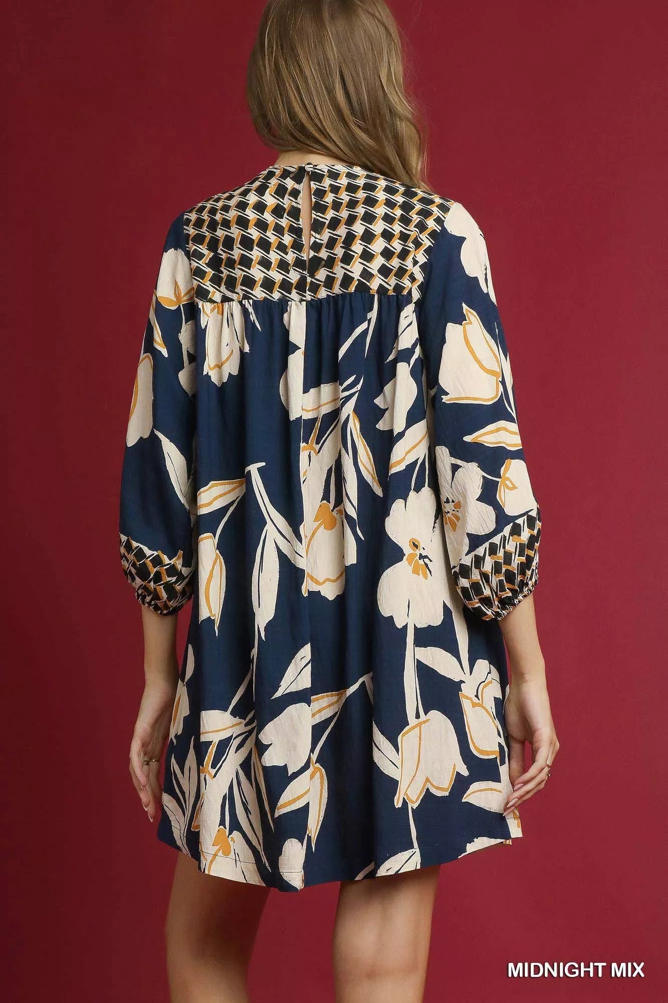 Rear view of navy floral high-low babydoll dress with checkered yoke and puffed sleeves.