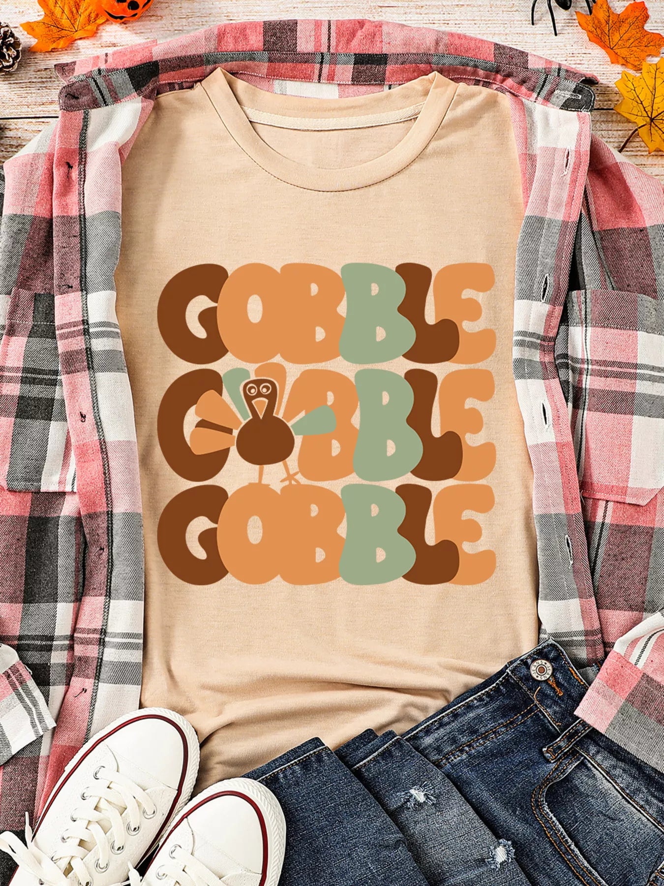 Beige round neck T-shirt with stacked "Gobble" text and turkey graphic, styled with plaid shirt and sneakers.