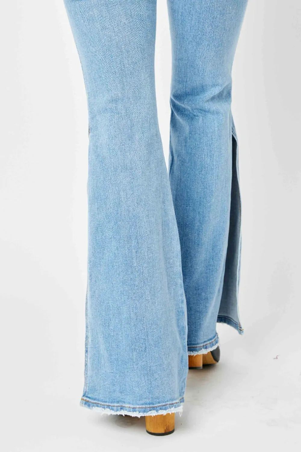 Light wash mid-rise raw hem flare jeans with side slit, viewed from behind.
