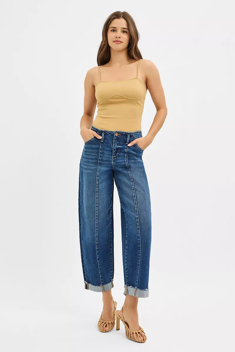 Model poses in RISEN high-rise barrel cuffed stretch denim jeans with raw hem.