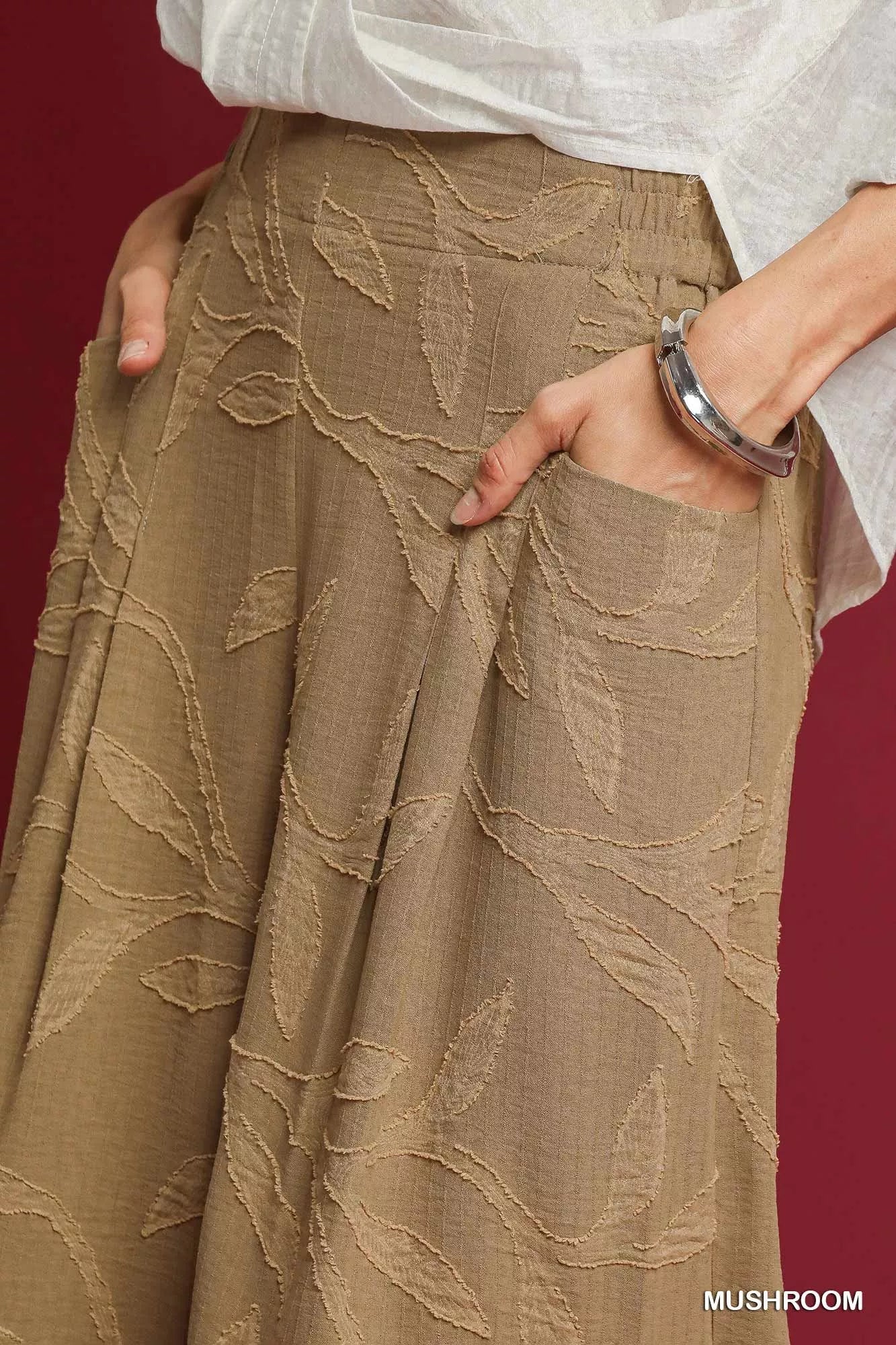 Beige jacquard wide-leg pants with leaf patterns and side pockets, paired with a white blouse.