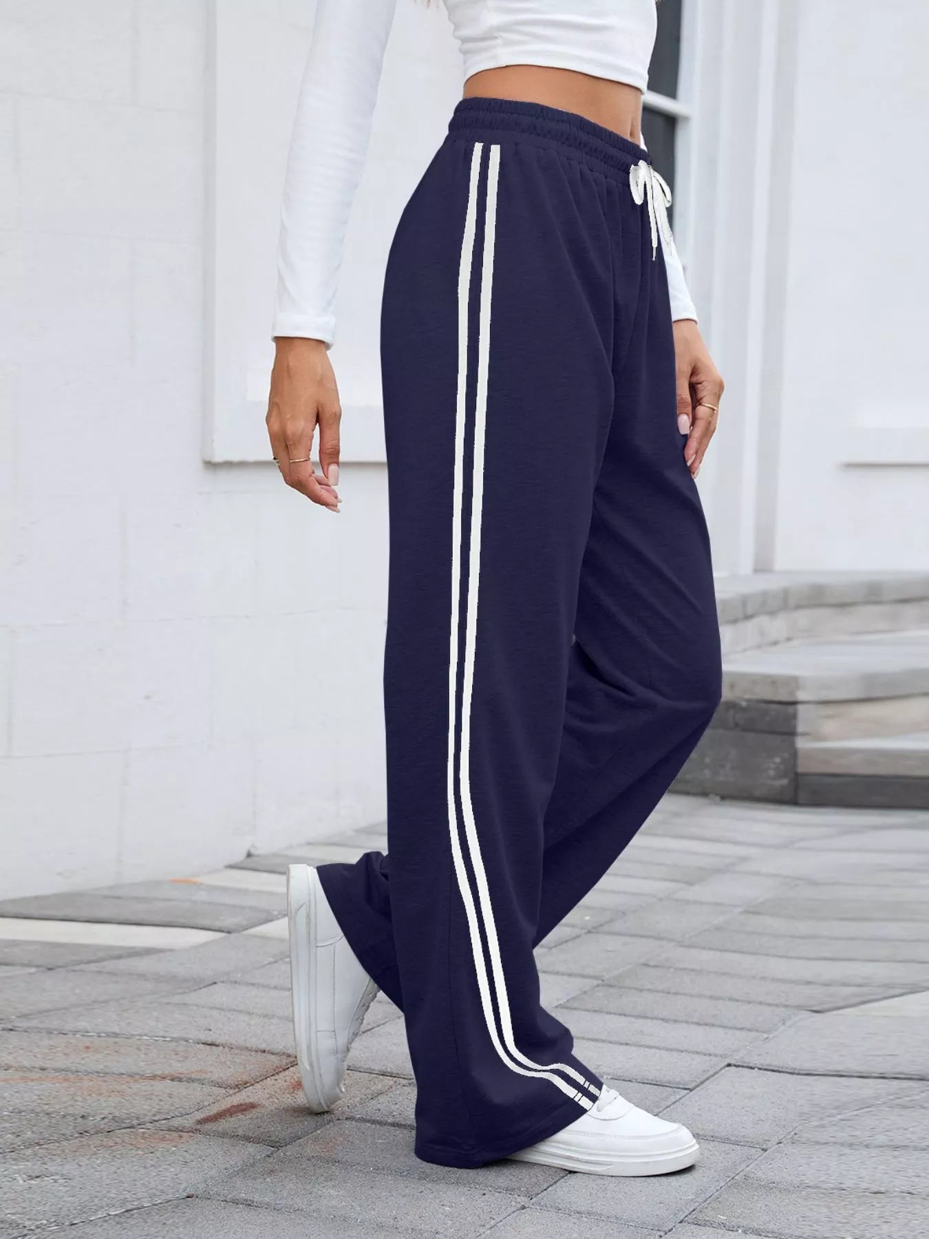 Model poses in navy wide-leg pants with white side stripes and drawstring waist.