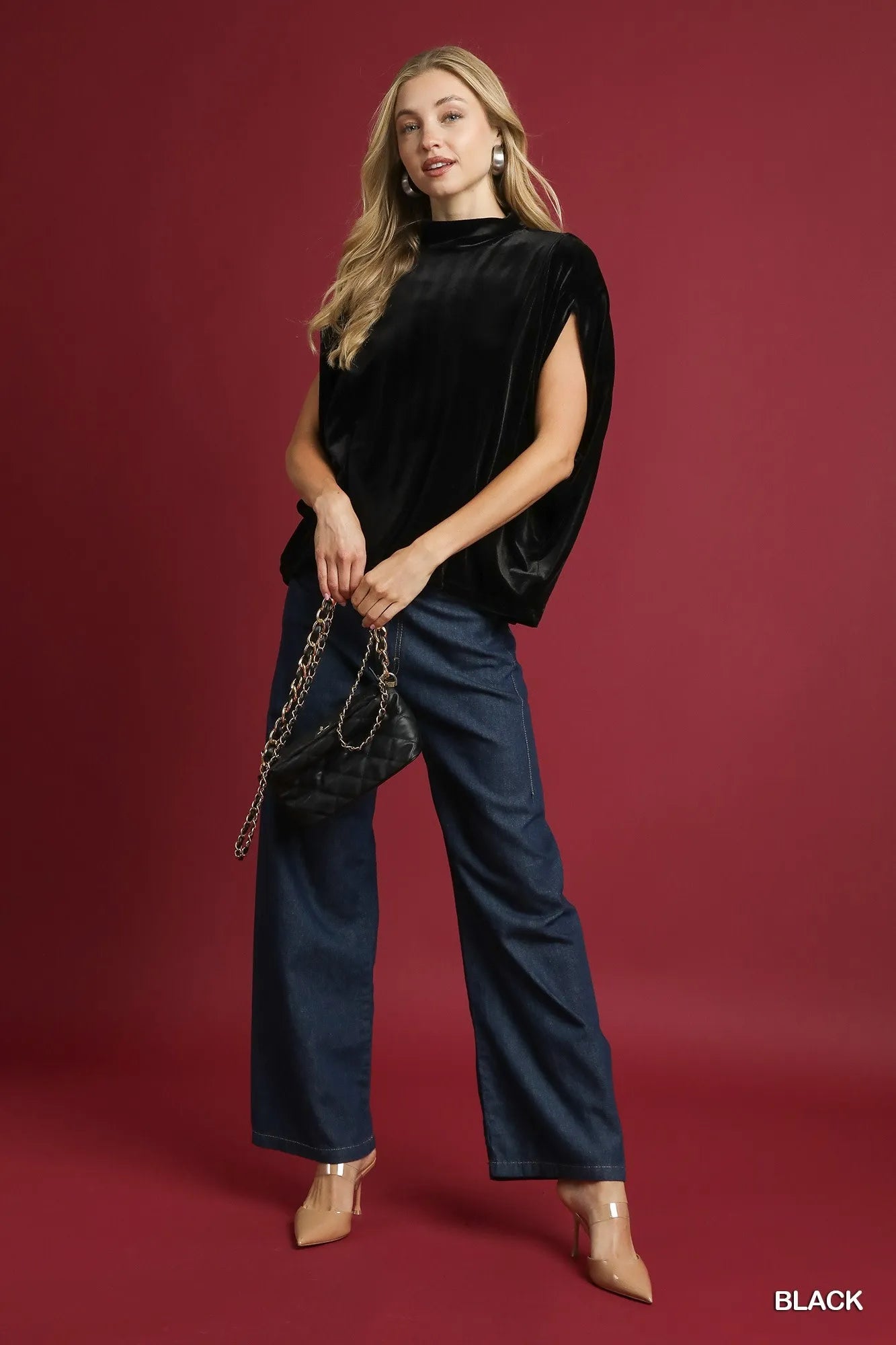 Model poses in black velvet mock neck sleeveless blouse with wide-leg pants and chain bag.
