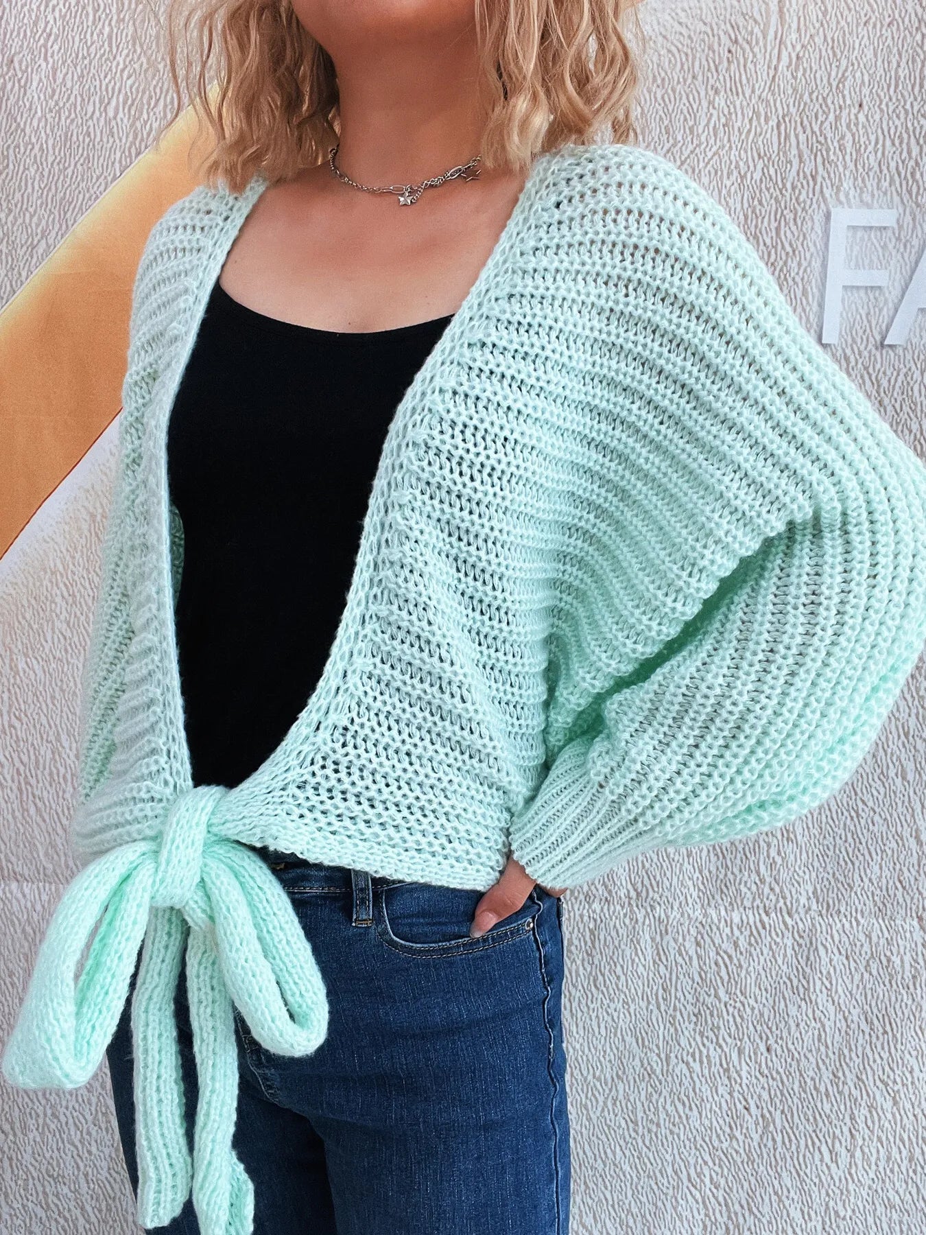 Light blue long-sleeve cardigan with tie front, worn open over black top and jeans.