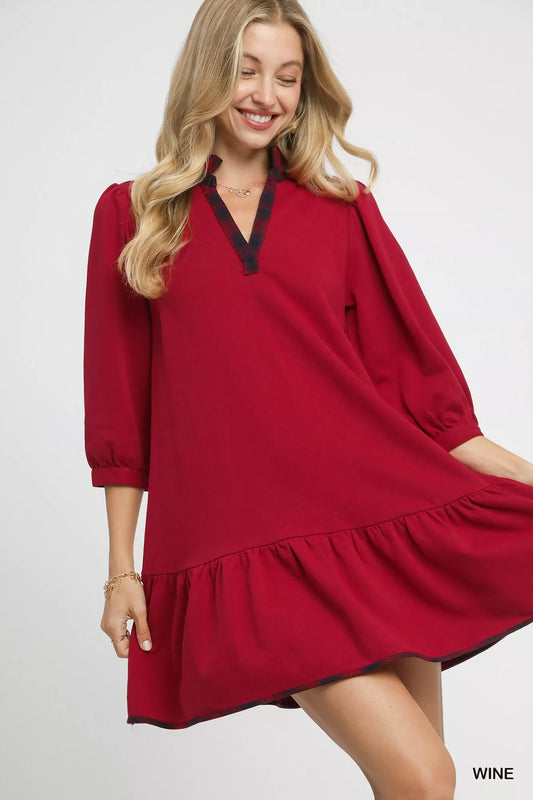Woman modeling red French terry ruffle hem dress with black plaid trim.